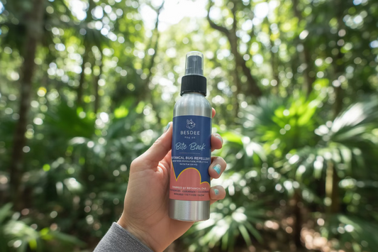 Hand holding a bottle of Besdee Bite Back botanical bug repellent in a casual indoor setting.